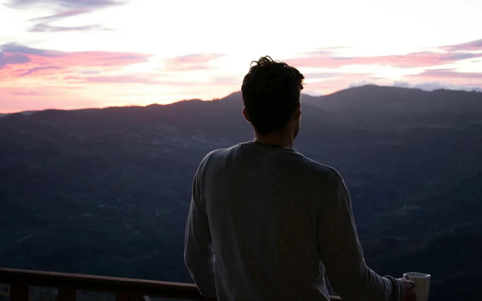 Homme avec une tasse de café sur un balcon, regardant les montagnes au lever du soleil
