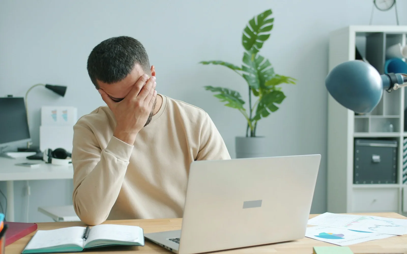 Homme qui se frotte les yeux de fatigue devant son ordinateur portable, dans un bureau lumineux