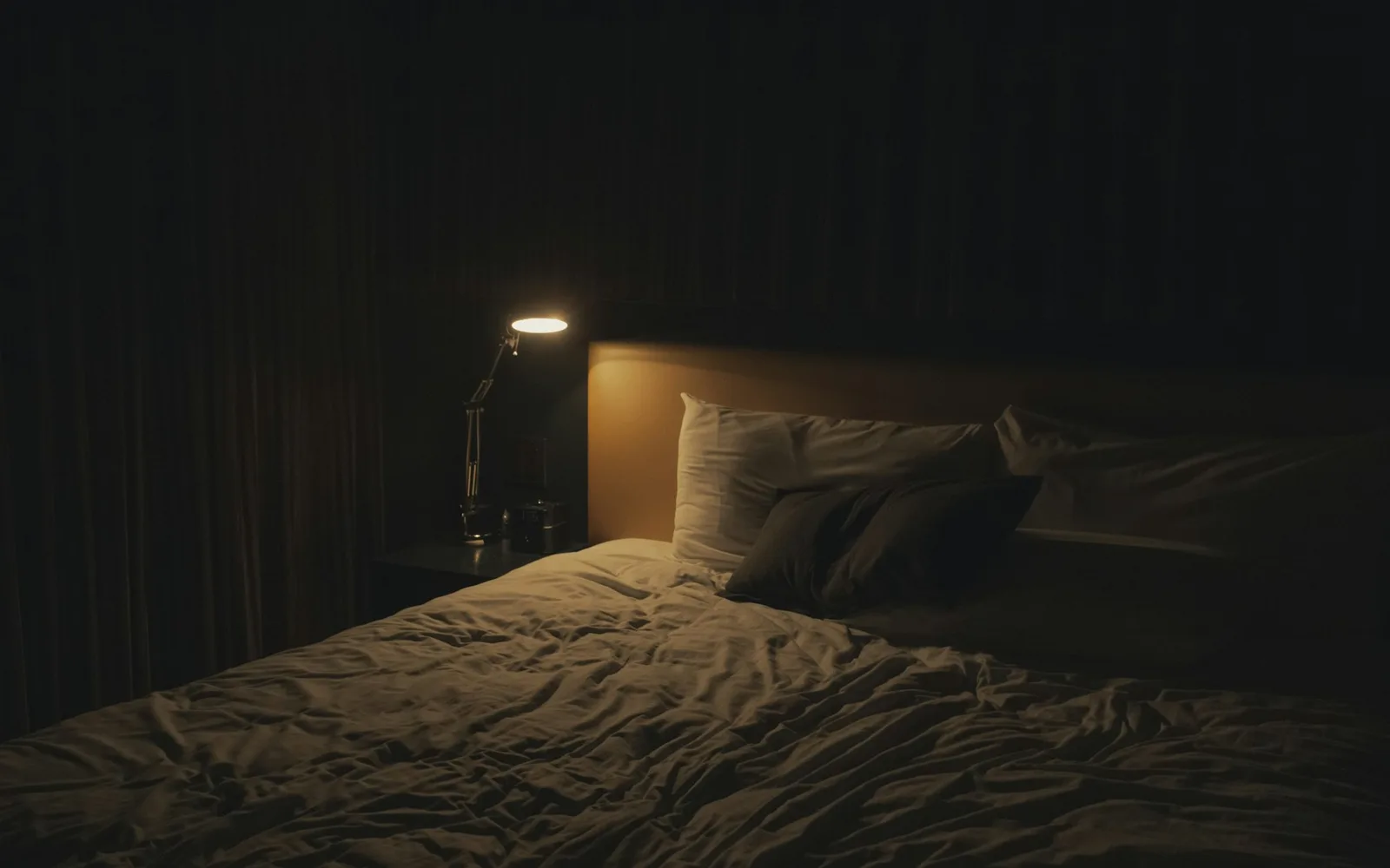 Lampe de chevet allumée dans une chambre sombre, à côté d'un lit