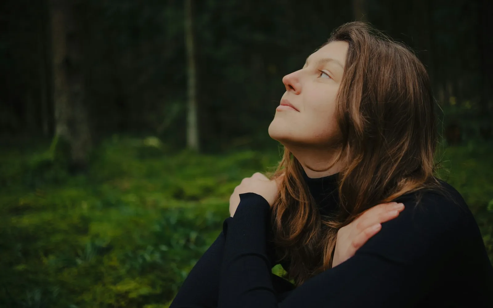 Femme les yeux fermés, les bras autour d'elle, qui respire calmement dans une forêt