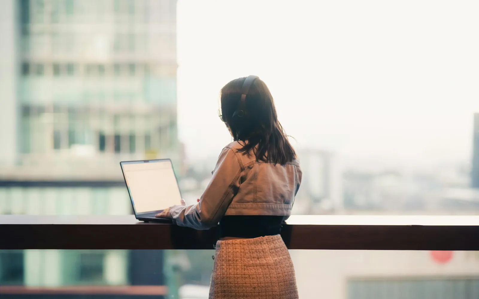 Femme d'affaires devant son ordinateur portable, regardant la ville par la fenêtre d'un bureau en hauteur